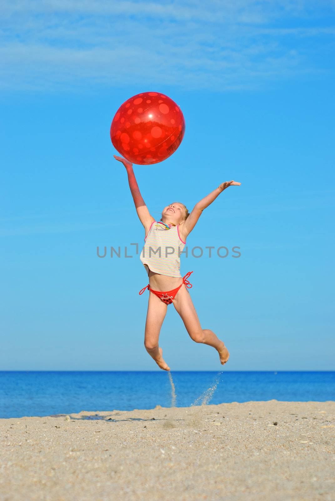 Jumping little girl with red ball on the beach