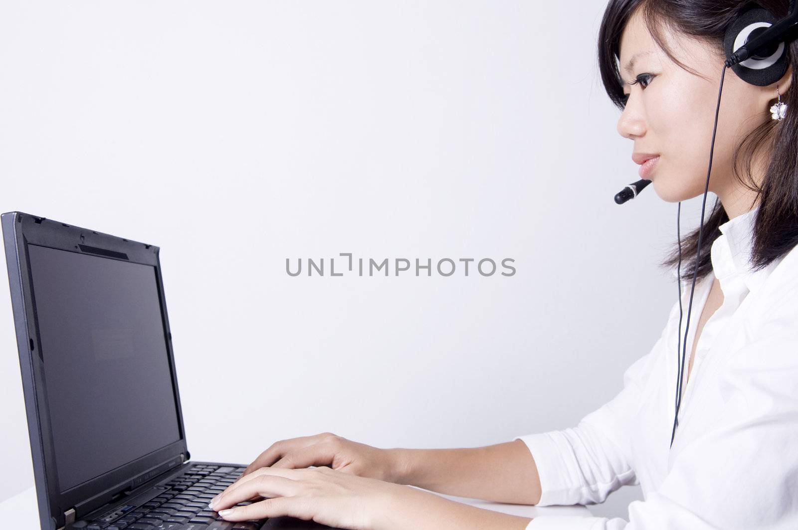 Asian consultants with headsets working on laptop computer on grey background. 