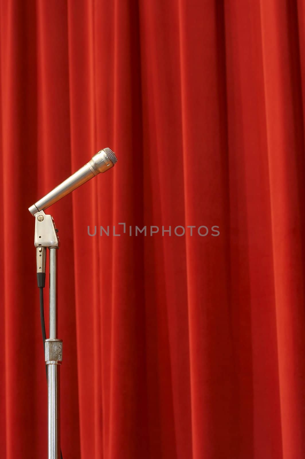 a crome microphone on a stage in front of a red curtain