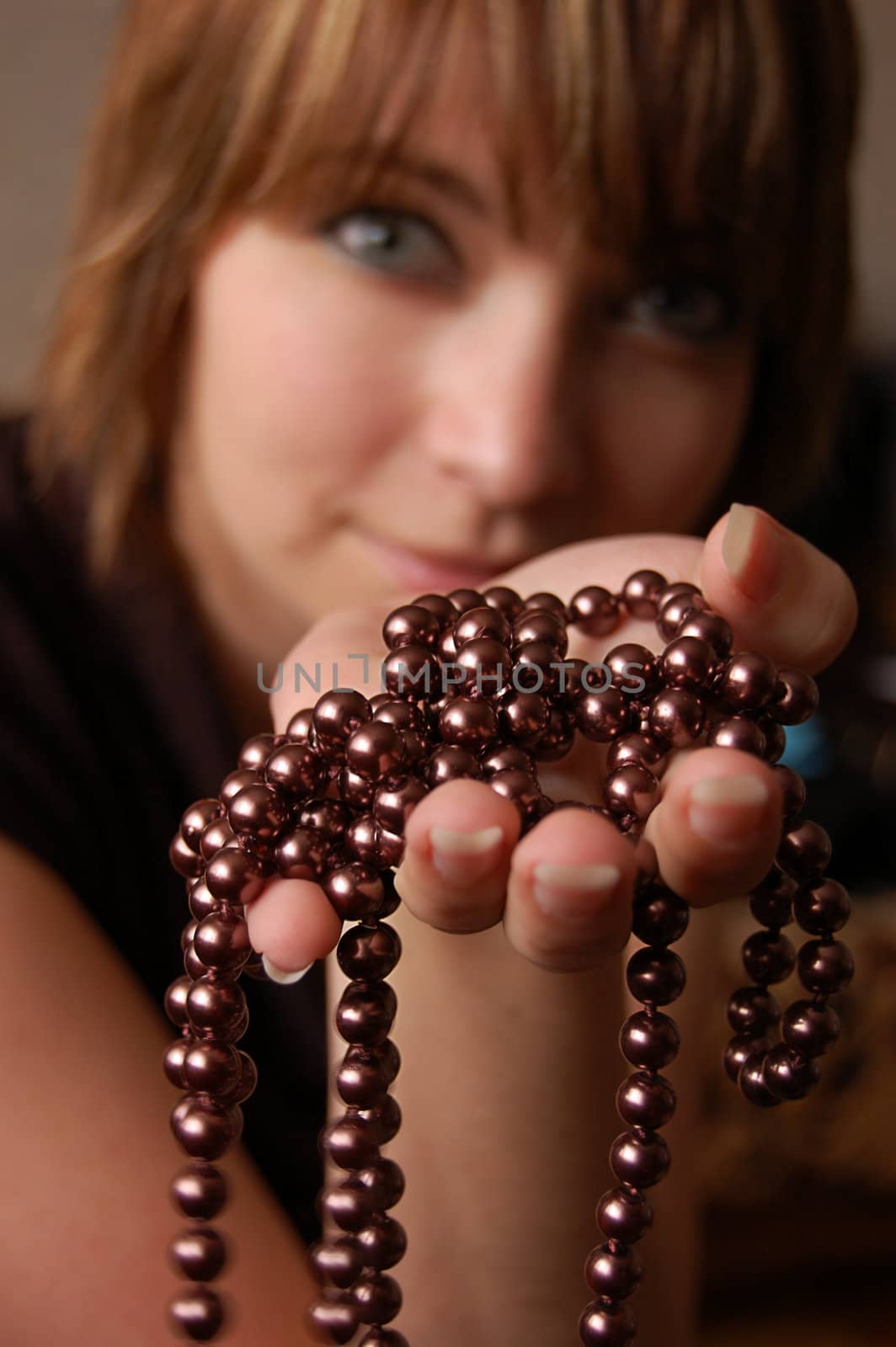 Girl holding brown pearl necklace, focus on hand