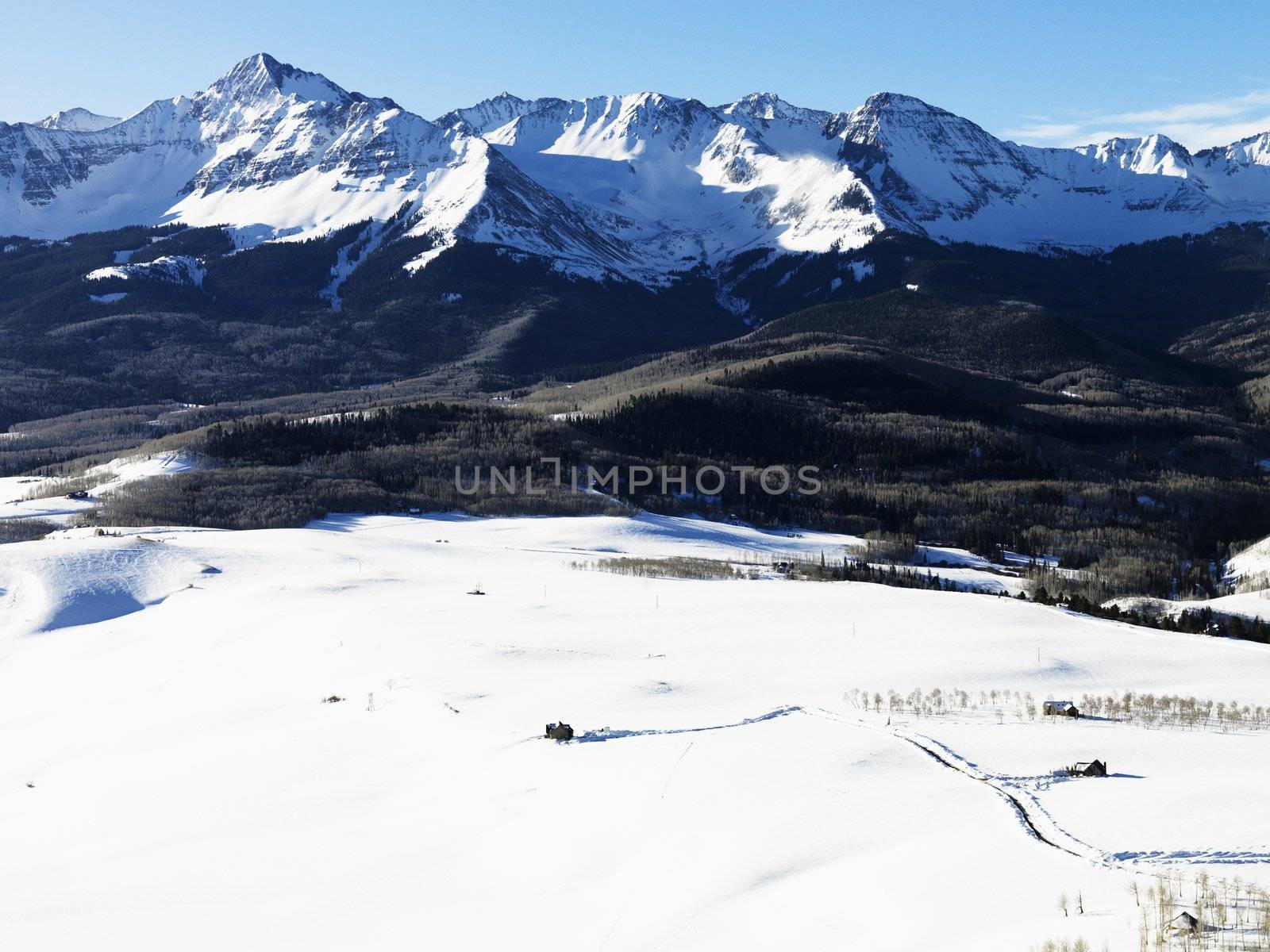 Aerial landscape of Colorado Rockies with snow covered valley in foreground.