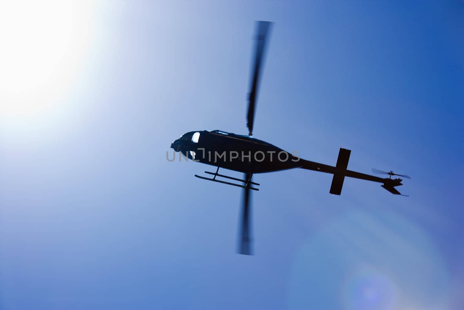 Low angle motion shot of helicopter flying overhead through blue sky.