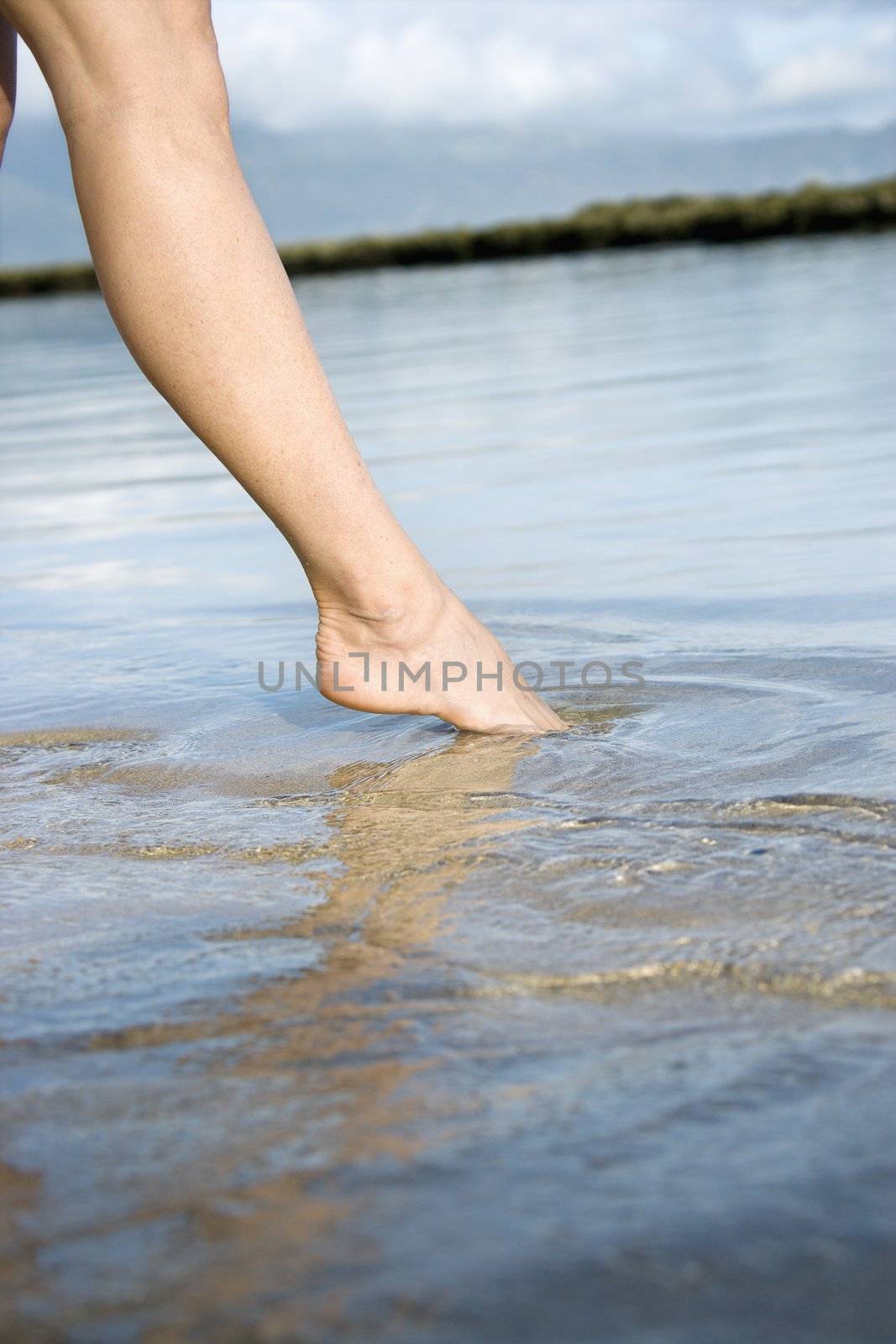 Woman dipping toe in water. by iofoto