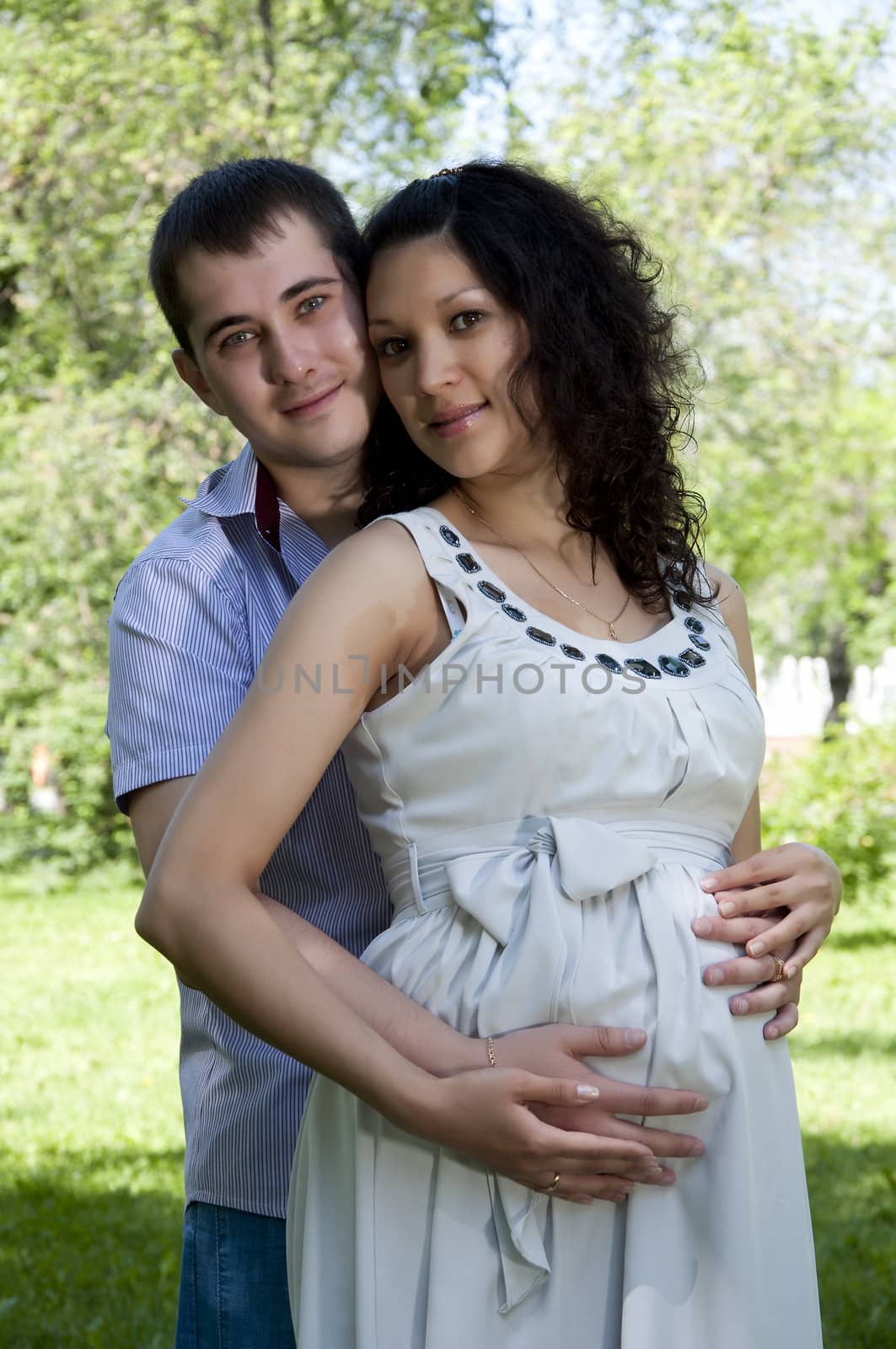 Man and a pregnant woman hugging in summer park