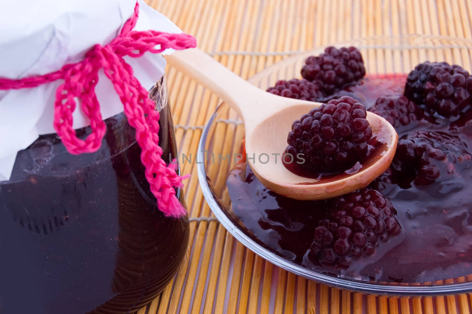 Blackberry jam in bowl and in plate on wooden spoon, focus on berry in plate