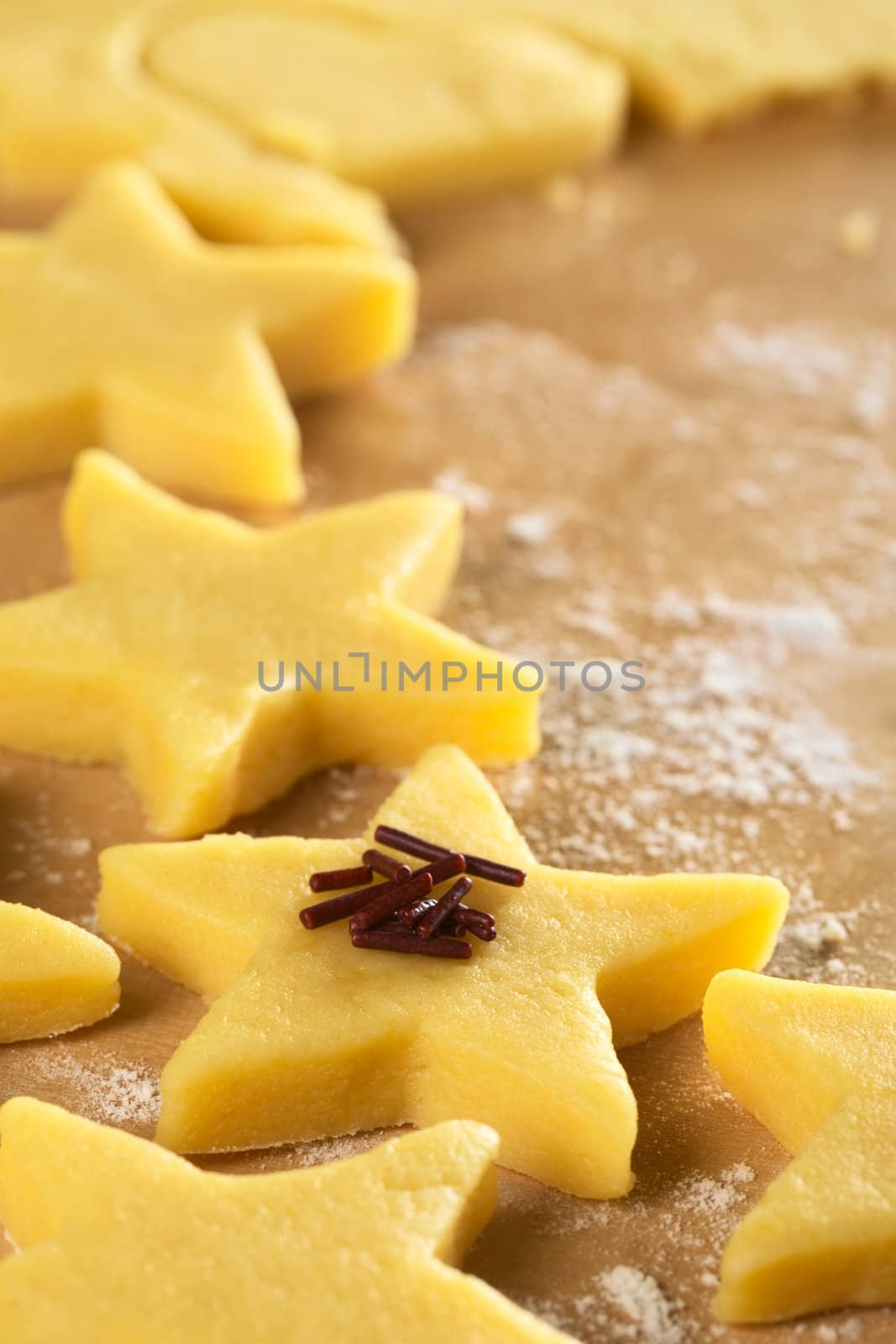 Unbaked star-shaped cookies with chocolate sprinkles on floured wooden surface (Selective Focus, Focus on the front of the chocolate sprinkles)