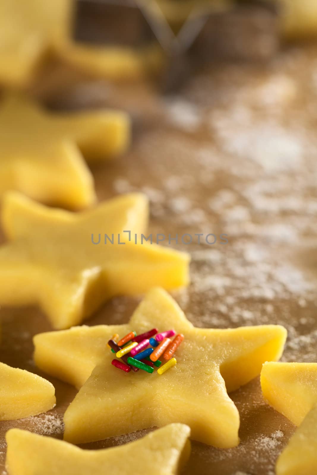 Unbaked star-shaped cookies with colorful sugar sprinkles on floured wooden surface (Selective Focus, Focus on the front of the colorful sprinkles)