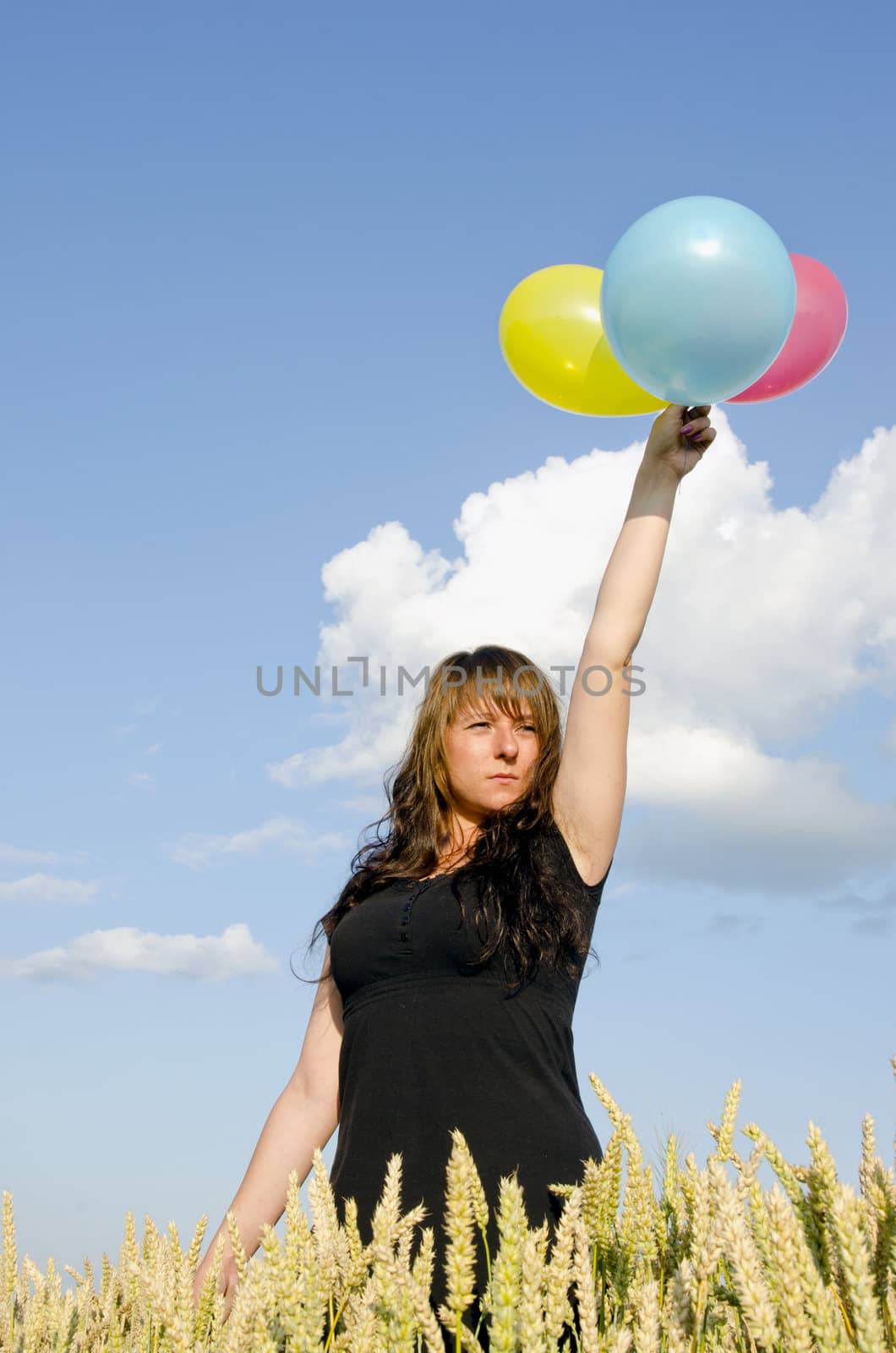 Young woman holding three different colored balloons in the field of wheat.