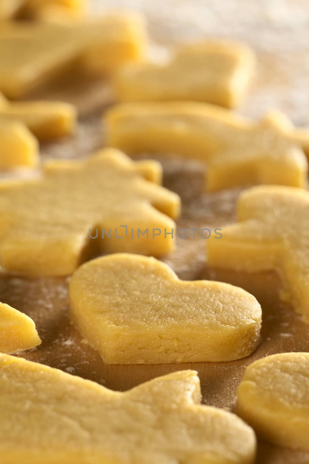 Unbaked Christmas cookies on floured wooden surface (Selective Focus, Focus on the front upper edge of the heart shaped cookie)