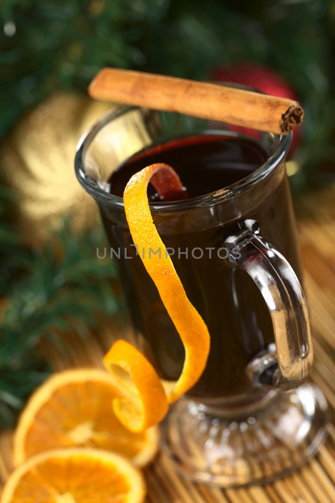 Hot spiced mulled wine garnished with orange peel and cinnamon stick (Selective Focus, Focus on the front rim of the glass and the orange peel at the rim)