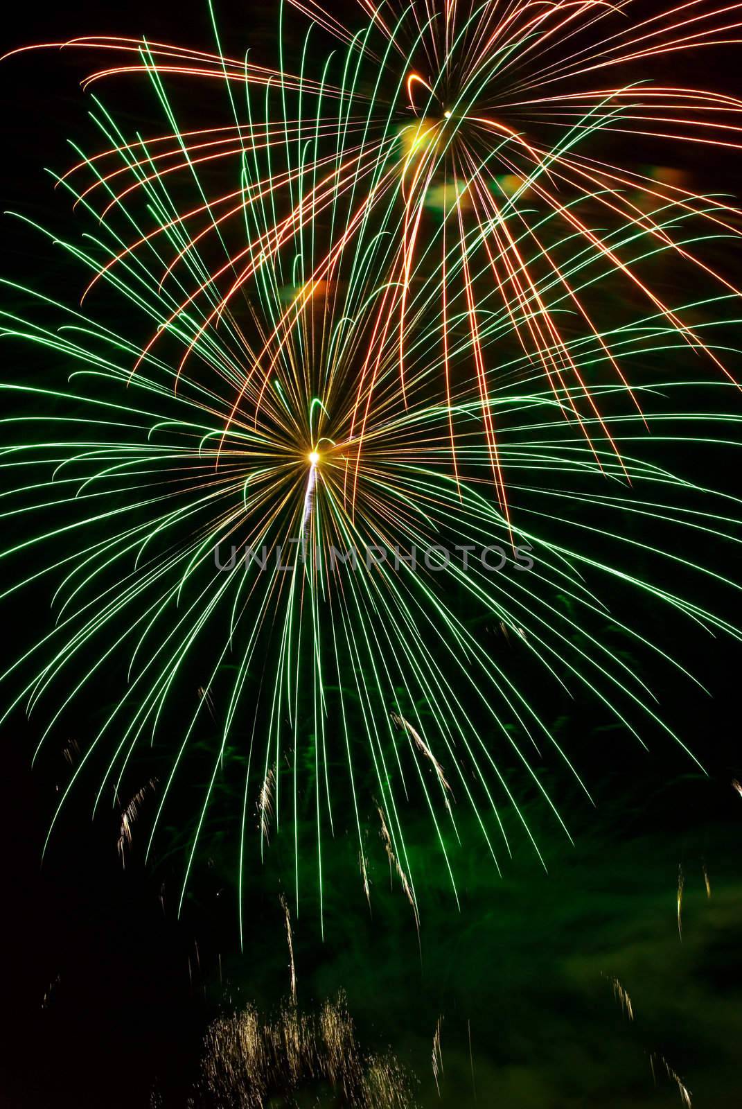 A green and orange burst of fireworks in the night sky.