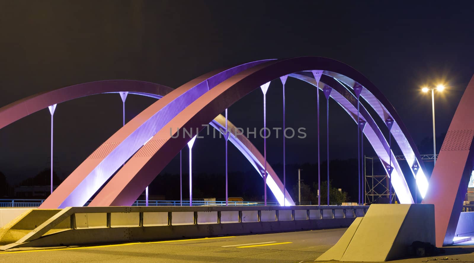 Pink steel girders of urban road bridge illuminated at night.