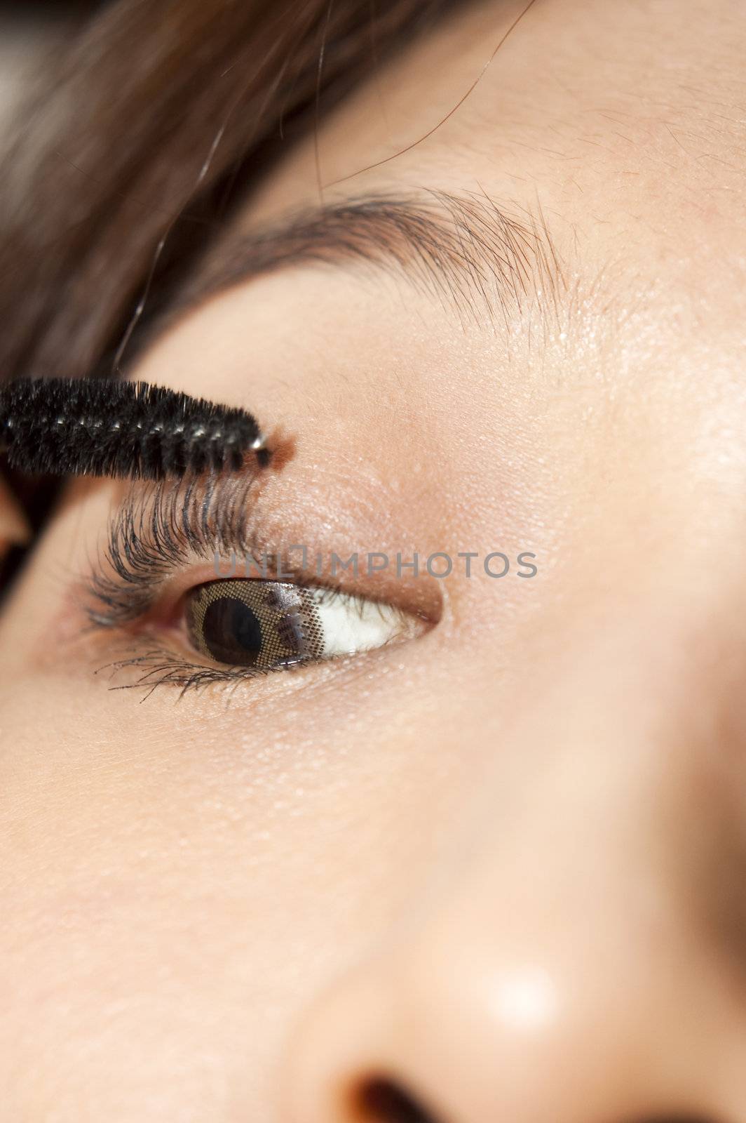 A young woman applying makeup, close-up on eye.