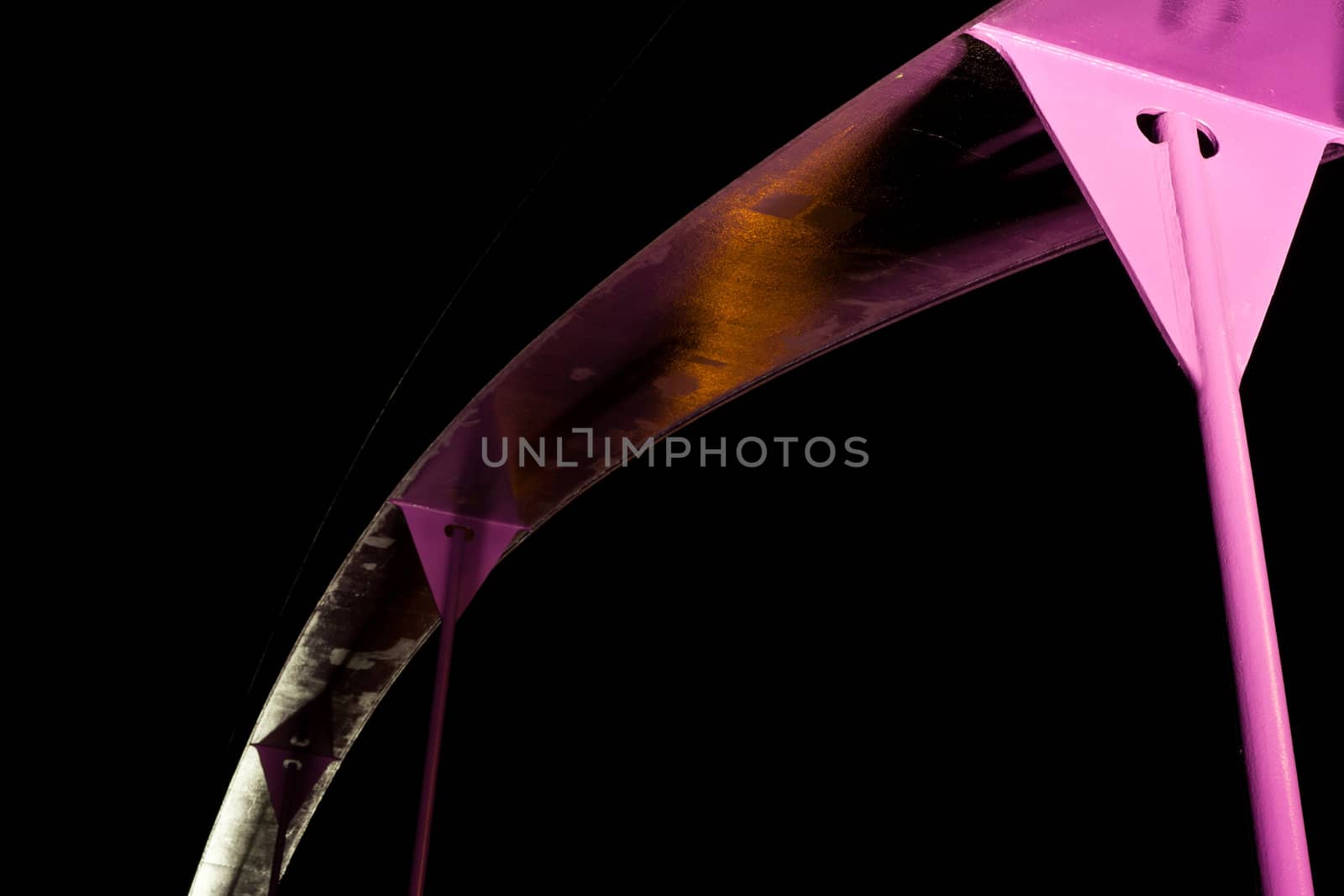 Detail of pink steel girder of urban road bridge illuminated at night.