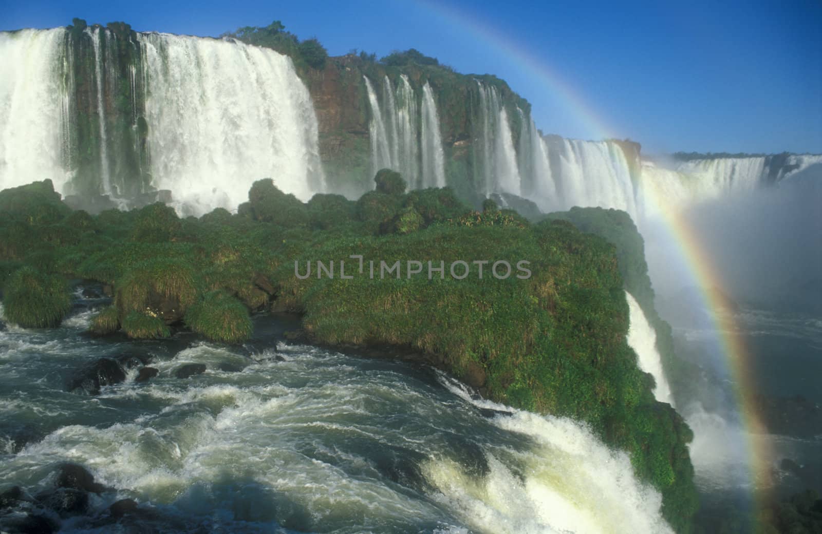 Large waterfalls with white water falling over cliff. Green vegitation and rainbow. Iguacu Falls, Brazil.