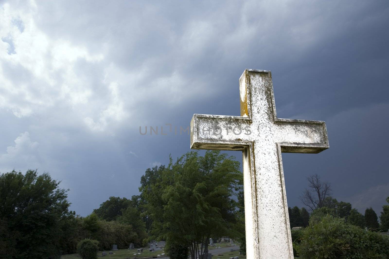 Cross in graveyard against stormy dark clouds in sky.