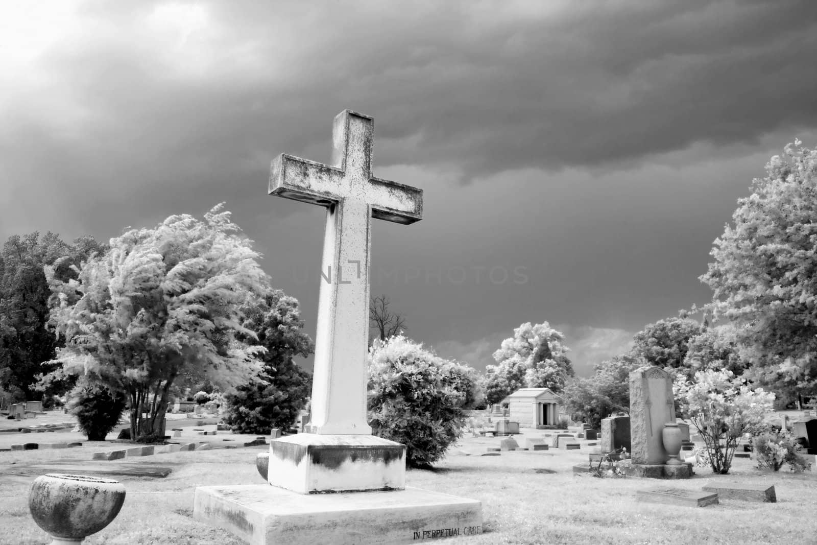 Infrared graveyard scene with cross and gravestones.