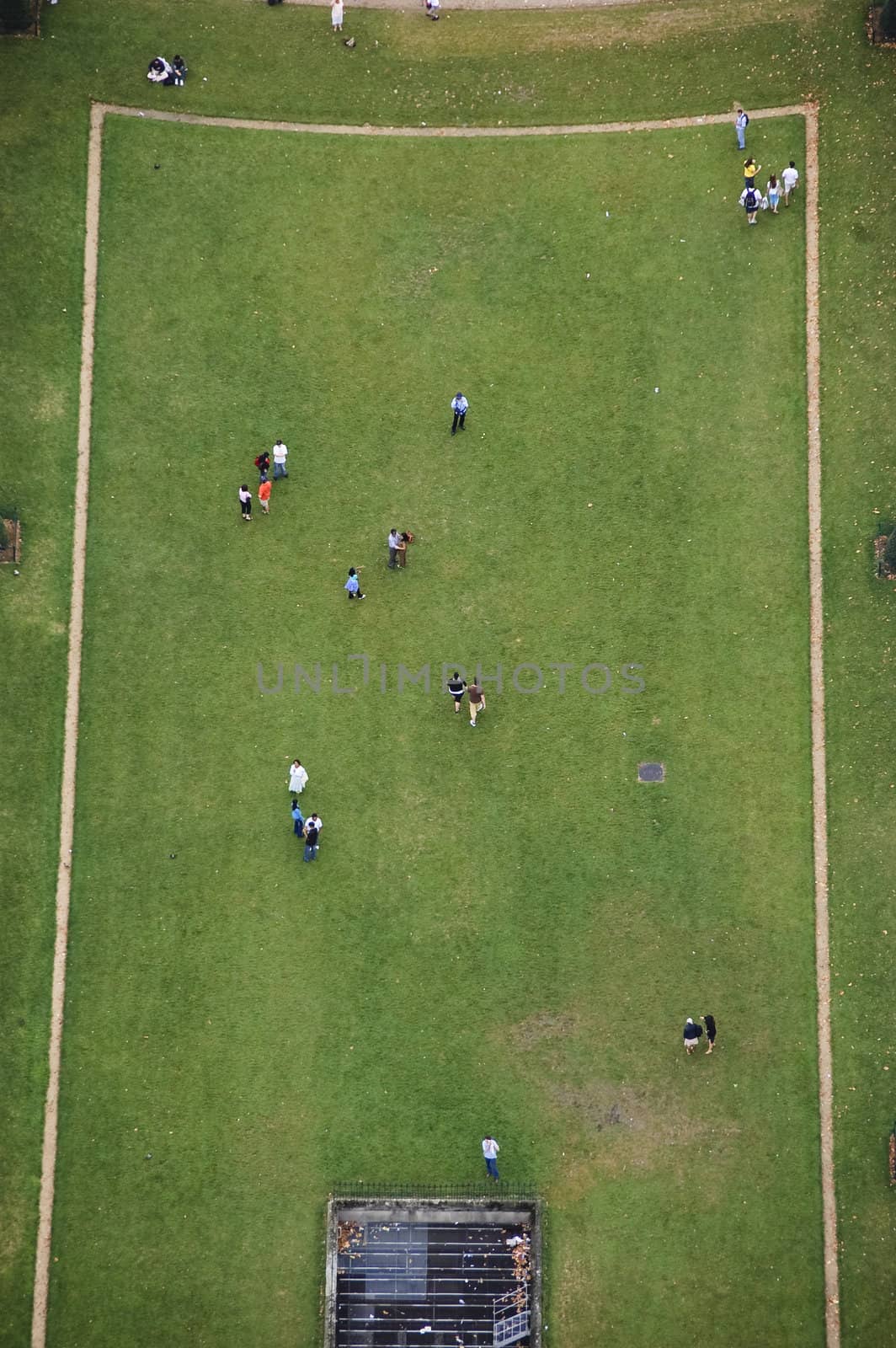 Bird's-eye view of section of Champ-de-Mars from top of Eiffel Tower showing grassy field with tourists walking on rectangular shaped area