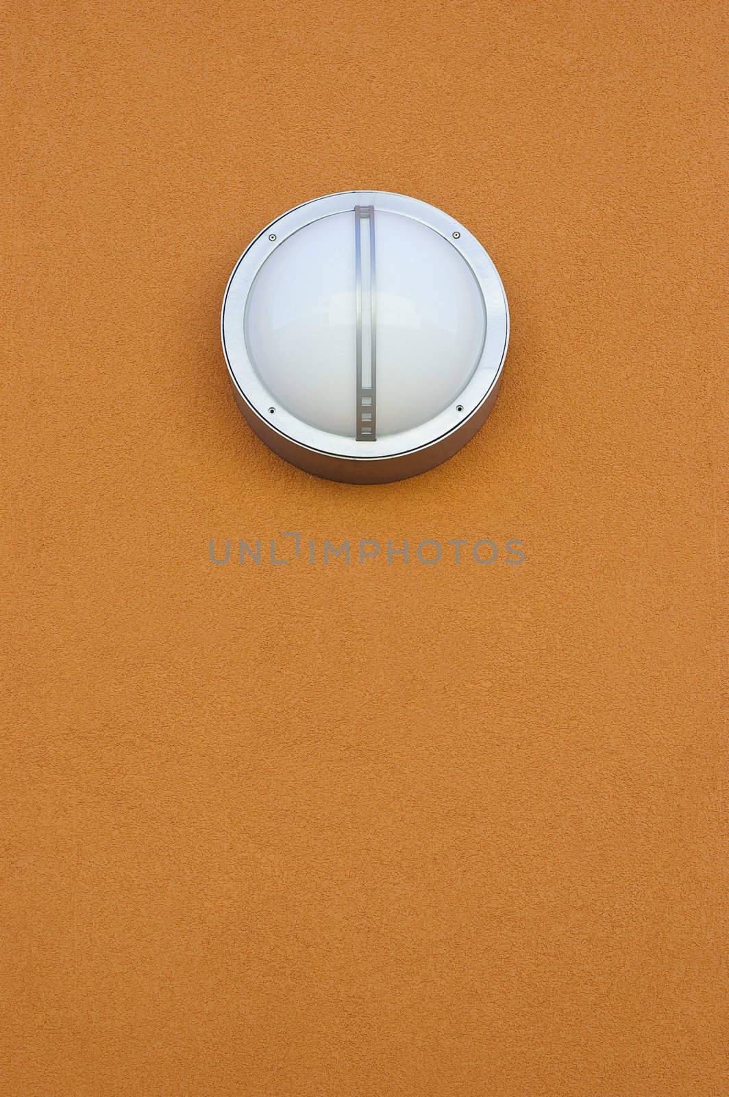 Round modern light fixture on orange stucco wall