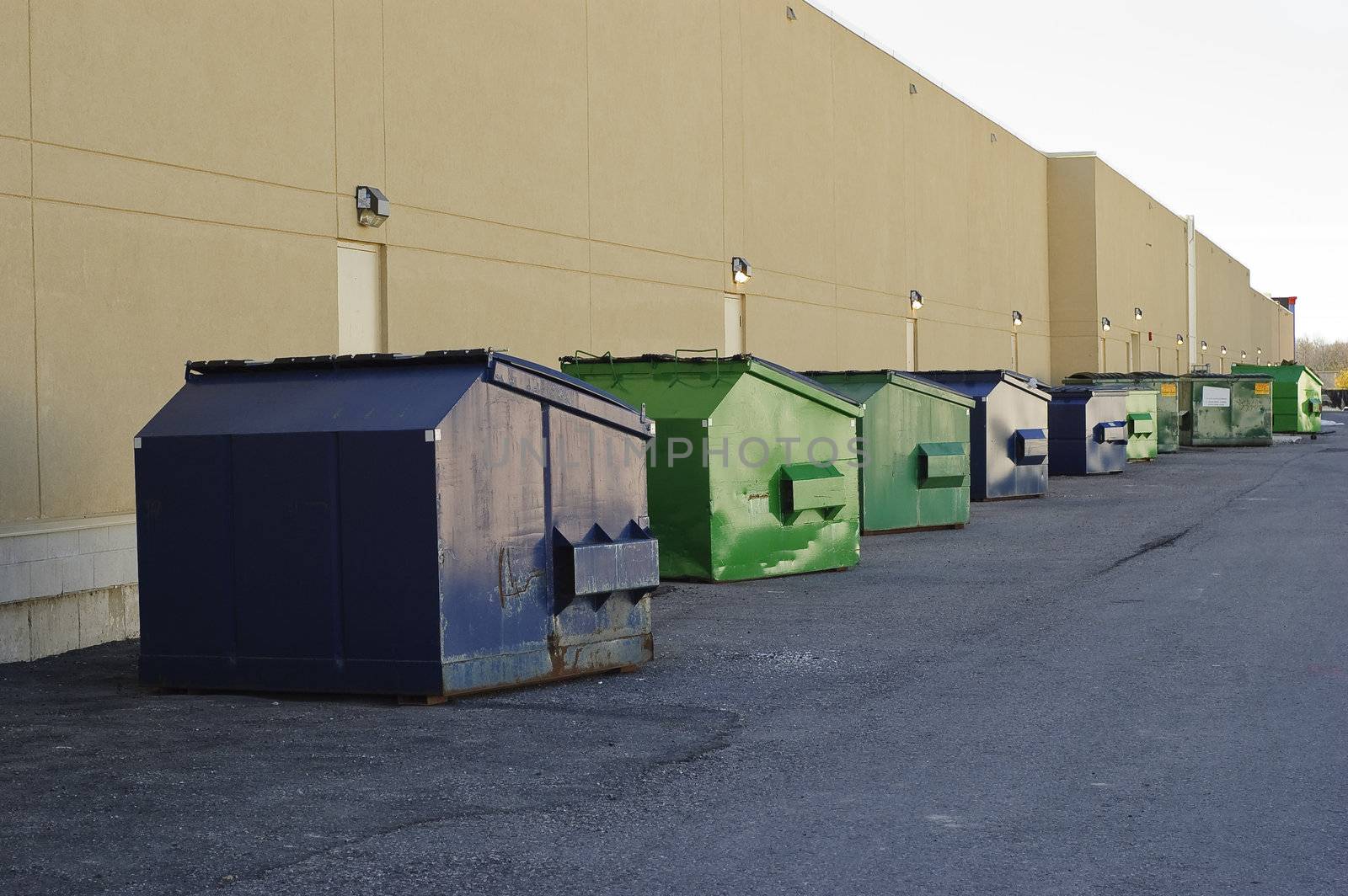 Blue and green industrial garbage bins lined up outside along commercial building