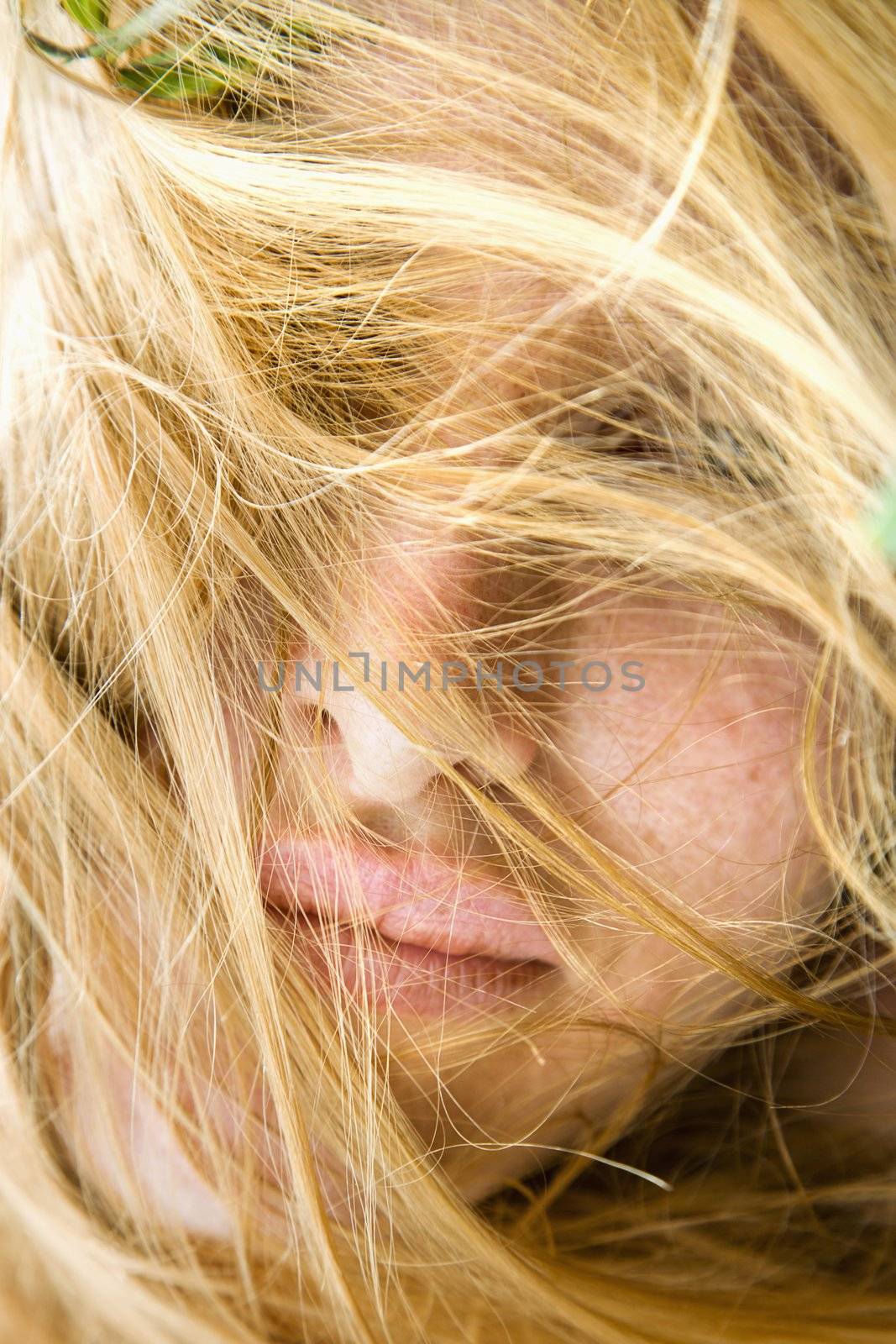 Close up portrait of redheaded woman with windblown hair covering face.