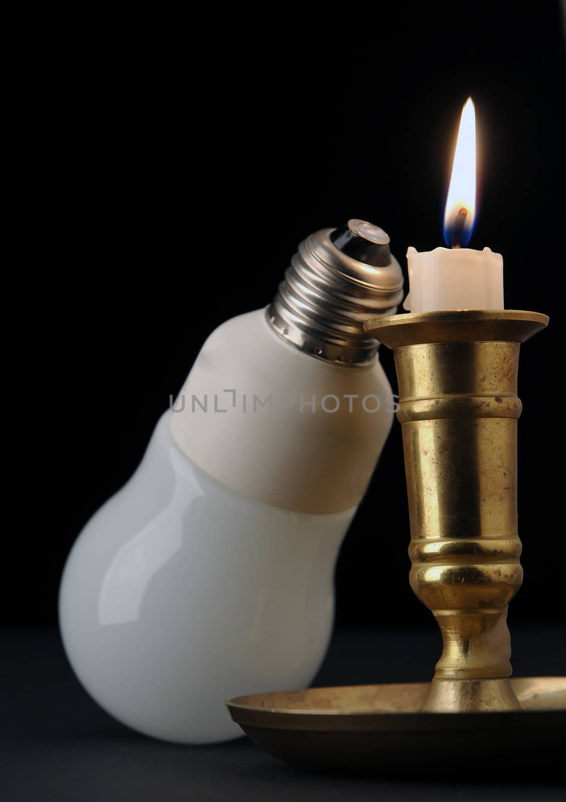 Aflame candle with modern bulb on black background