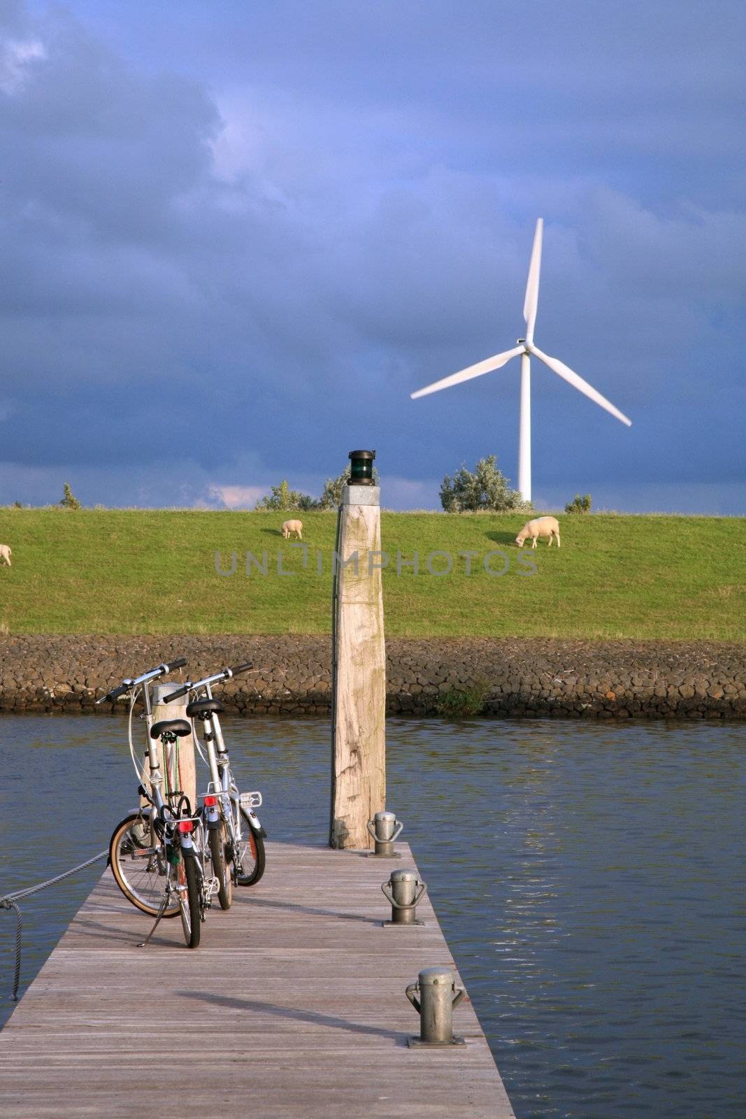 Eco-friendly means of transport and renewable energy. Bicycles above the canal and modern windmill by sunset.