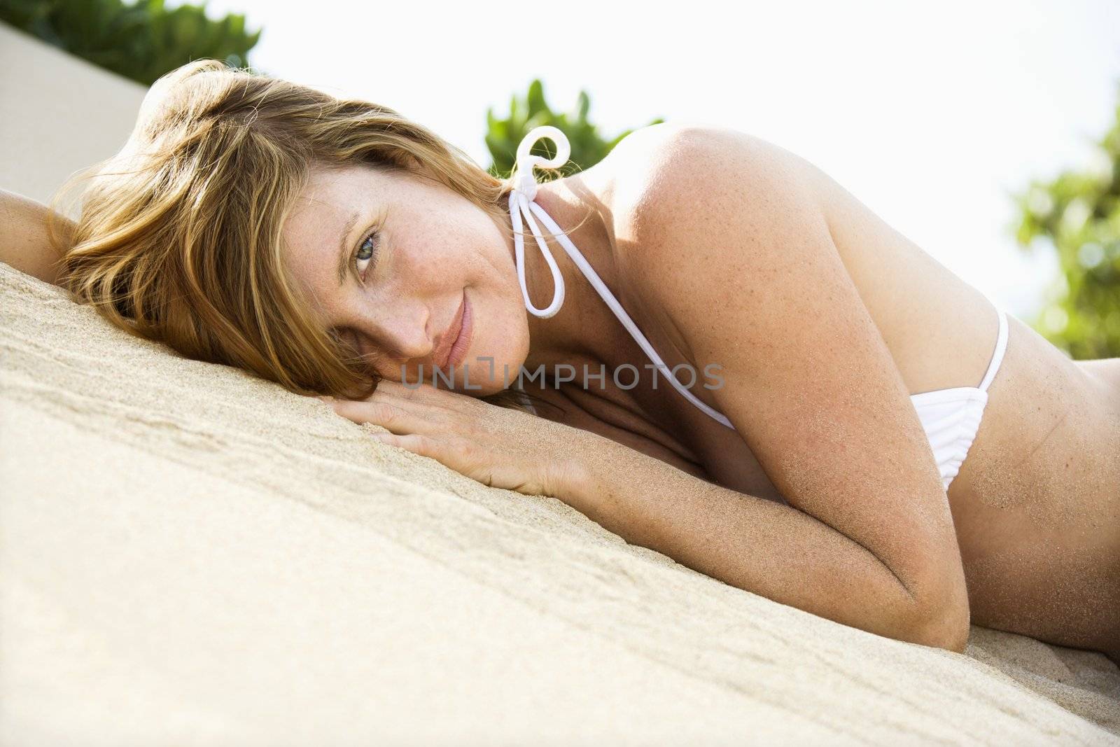 Portrait of pretty redheaded female lying in sand wearing bikini.