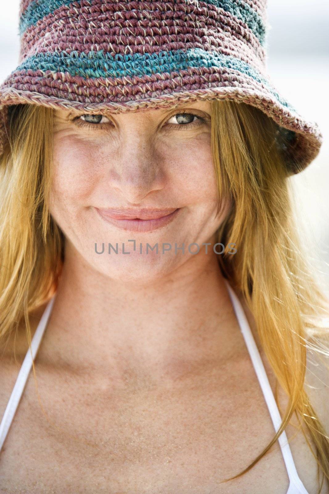 Close up portrait of smiling attractive young redheaded woman wearing hat and bikini top.