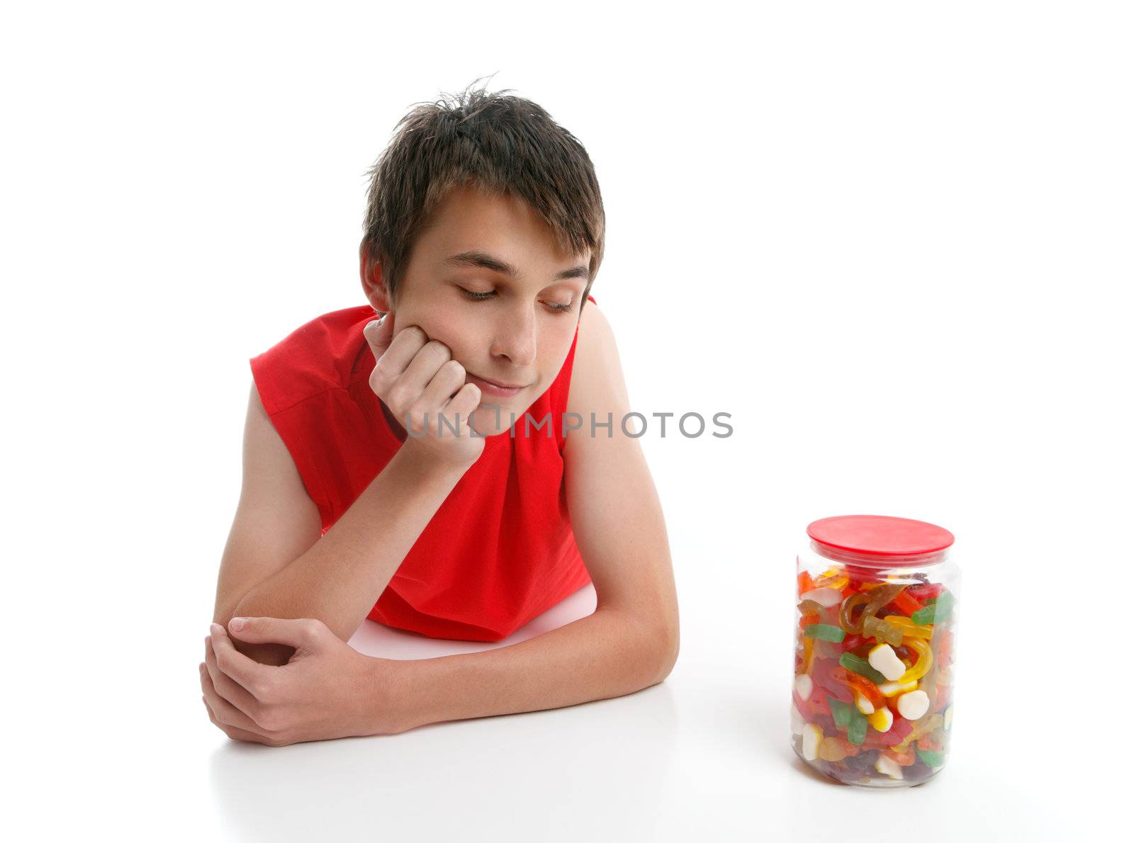 A boy ponders whether to open a jar of assorted confectionery.  White background.