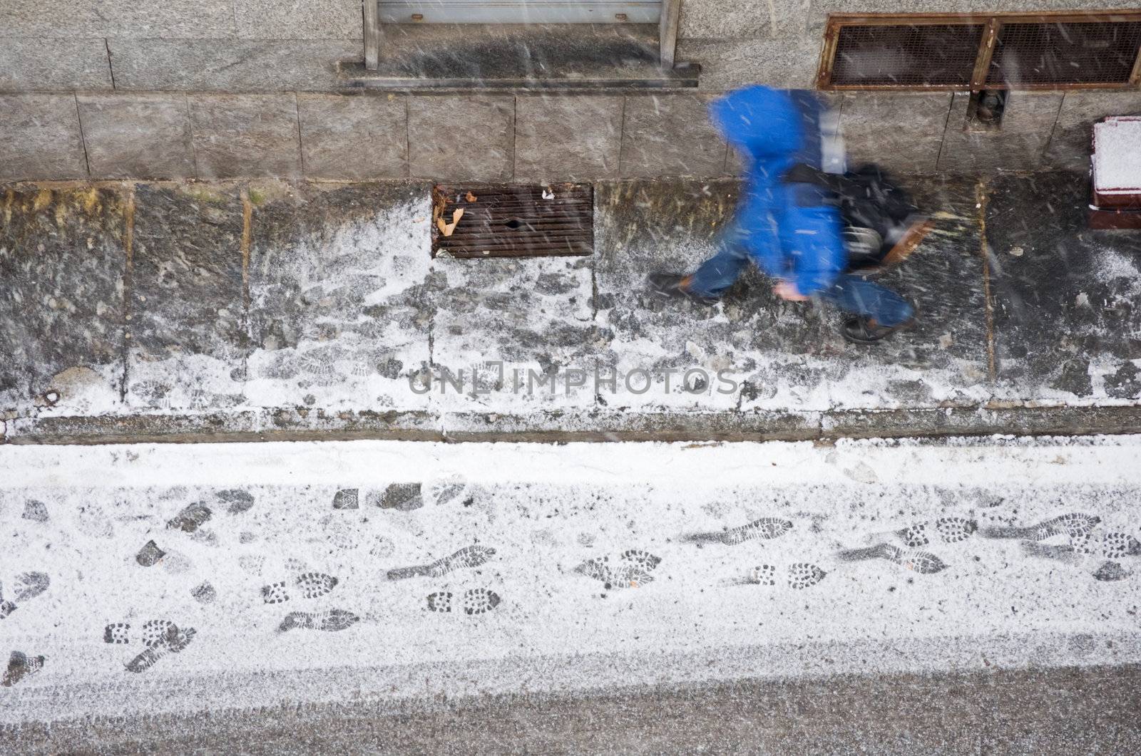 Passer by walking on a snowy day in a street. View from above.