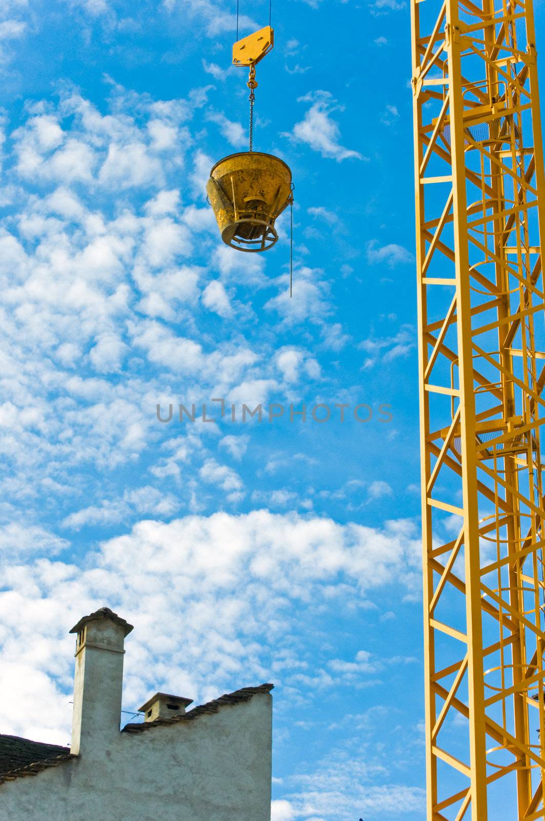 Yellow crane near building standing against blue sky with fluffy clouds.