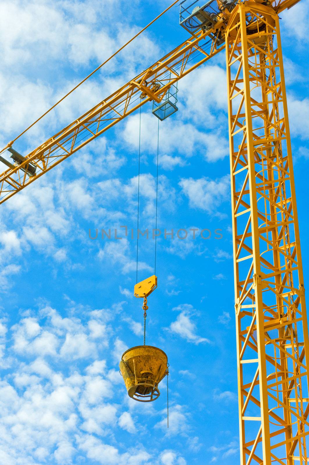 Yellow crane against blue sky with fluffy clouds.