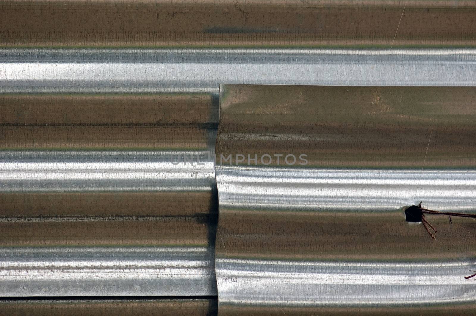 Layers of corrugated aluminum sheeting fence tied with rusty wire.