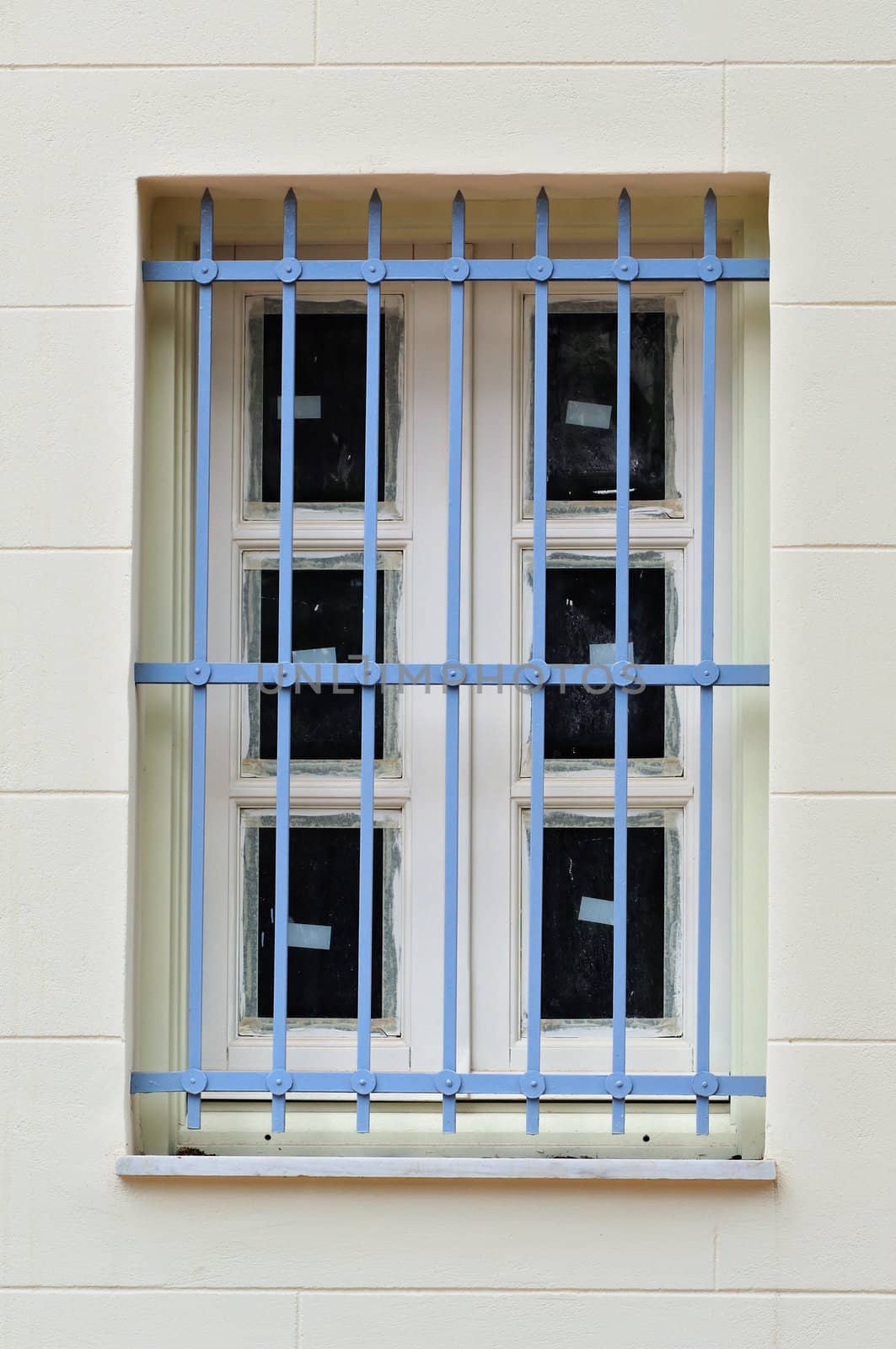 Protective metal bars and dirty window of a renovated building.