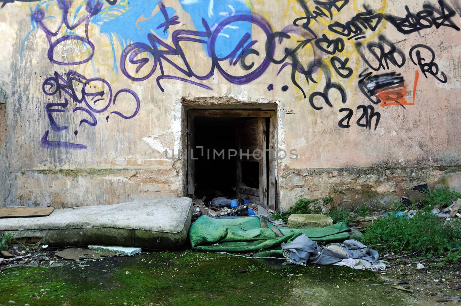 Dirty mattress and wooden pillow next to an abandoned house basement door.