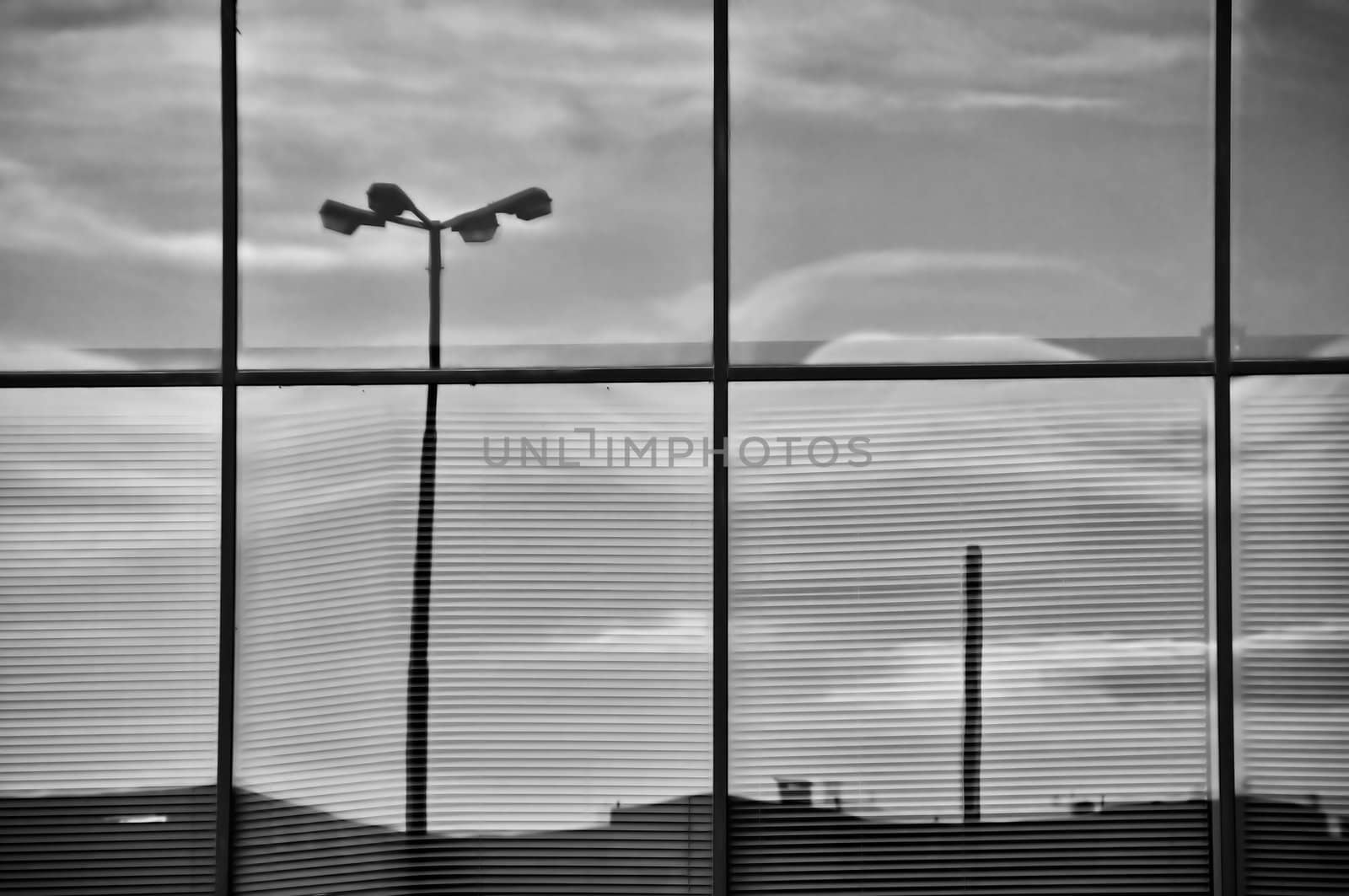 Overcast sky and street lights mirrored on the glass windows of a modern office building. Architectural detail.
