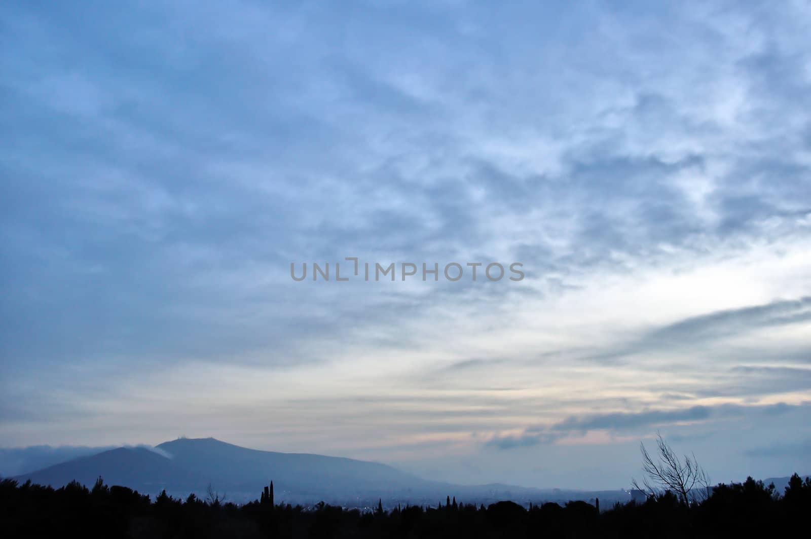 Distant city lights and foggy mountain horizon under sunset colored sky.