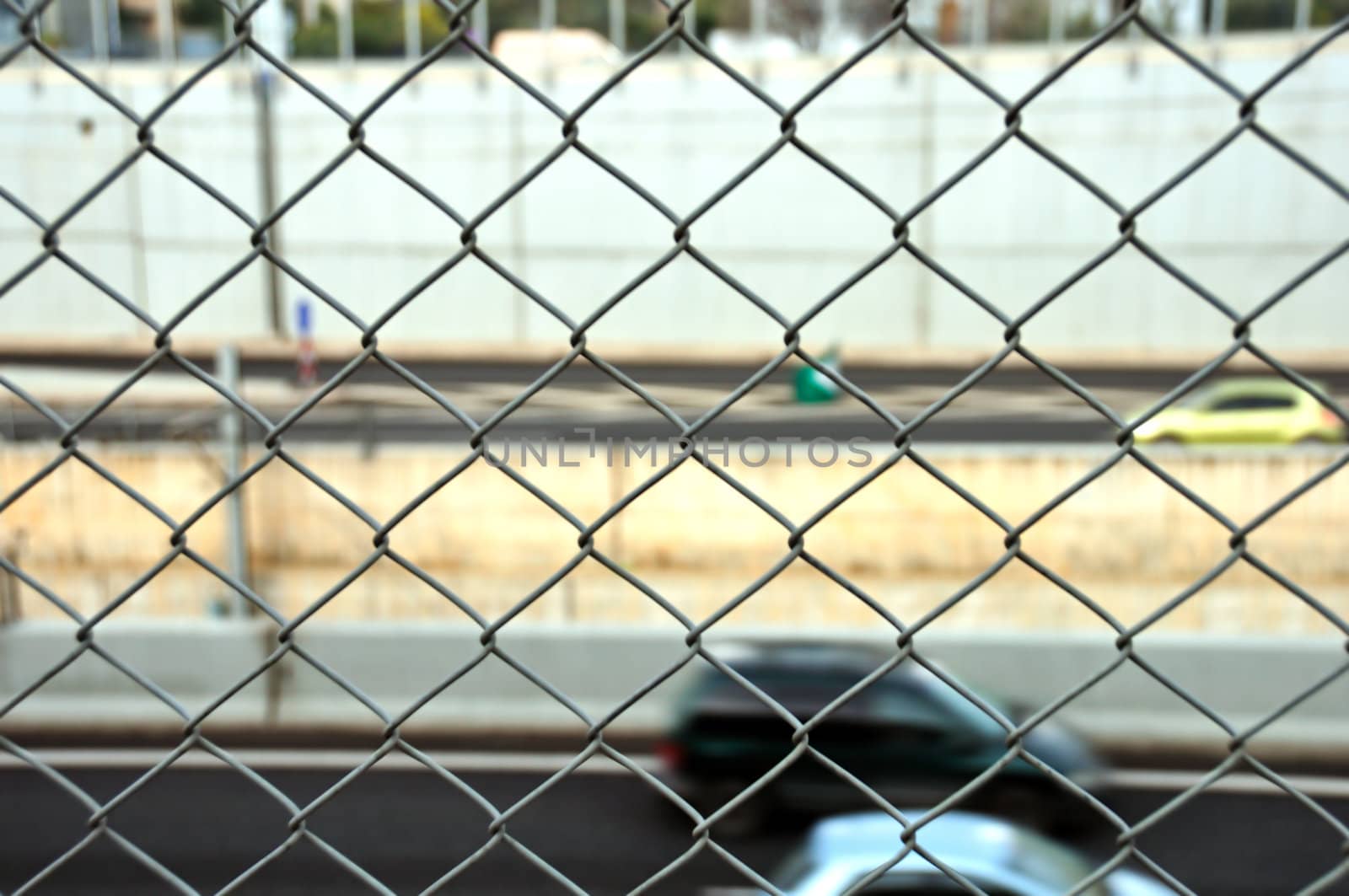 Speeding cars on the motorway seen through wire mesh fence. Motion blur.