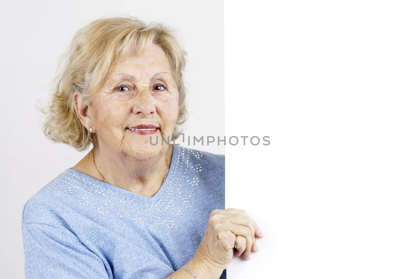 Friendly and smiling senior woman holding a blank white sign or placard ready for advertisement or information.