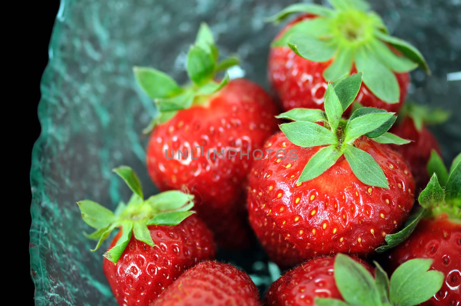 Glass bowl with fresh strawberries on black background. Selective focus macro.