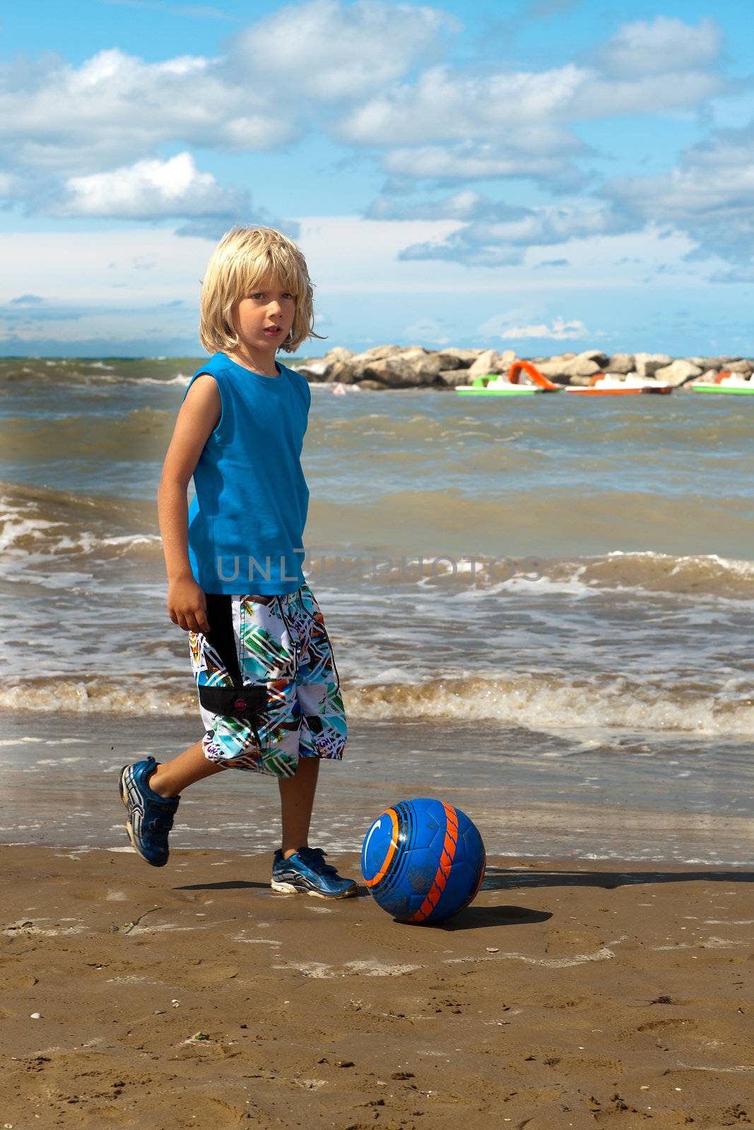 a boy is playing football on the beach on a sunny day