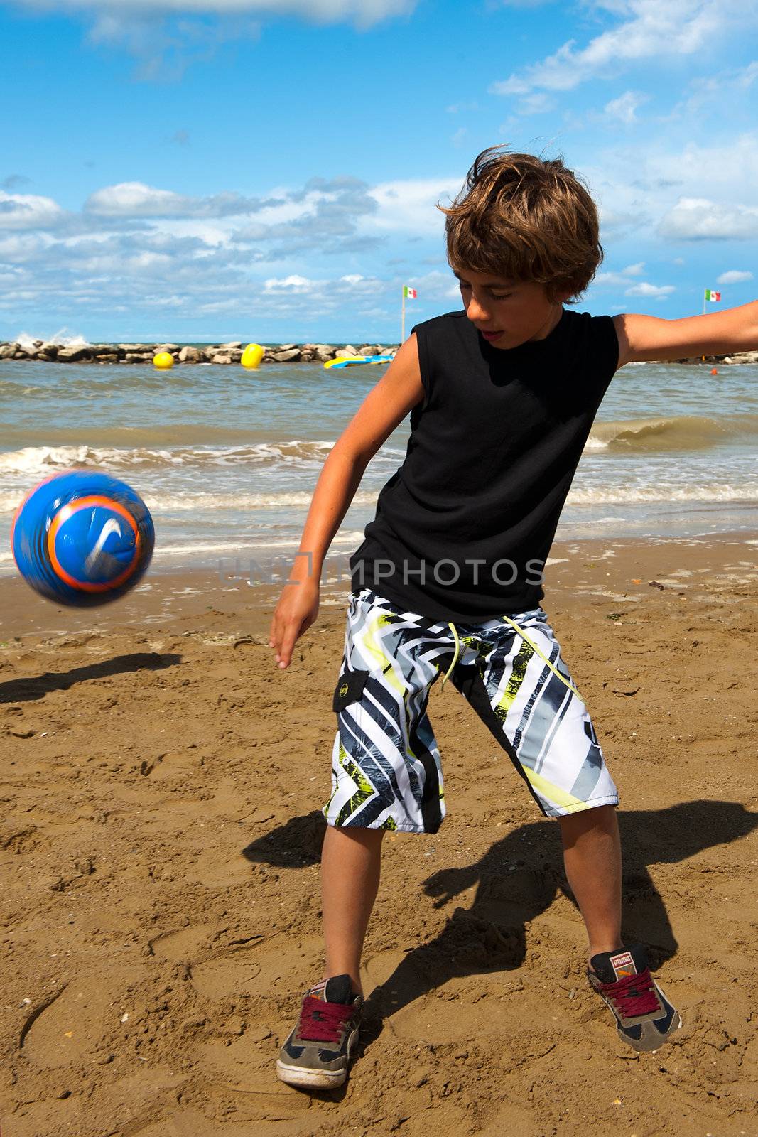 a boy is playing football on the beach on a sunny day