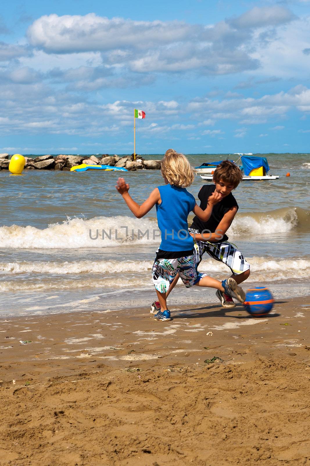 two boys playing football on the beach on a sunny day