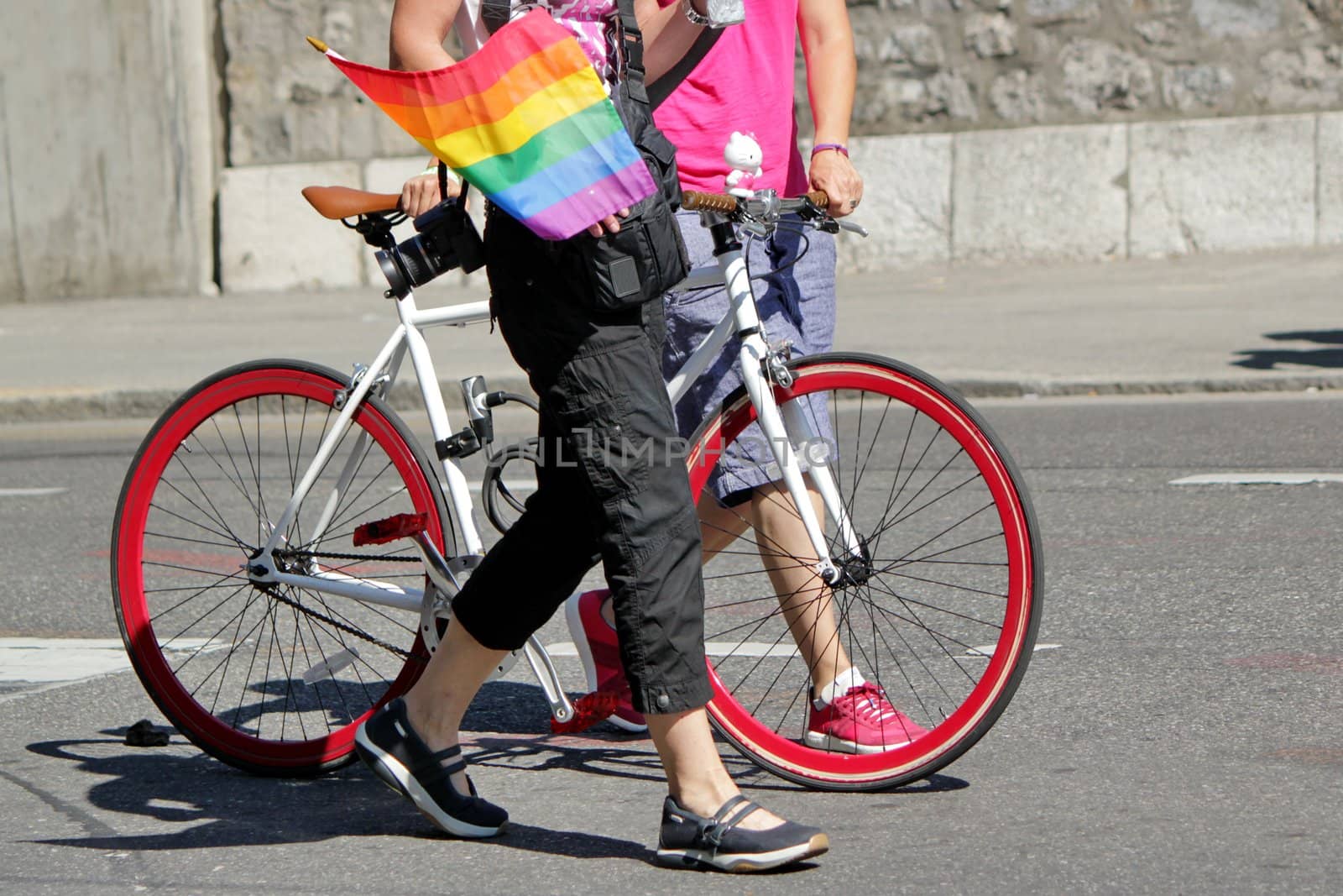 Two persons walking next to a red bicycle at the Gay Pride, one holding a rainbow flag