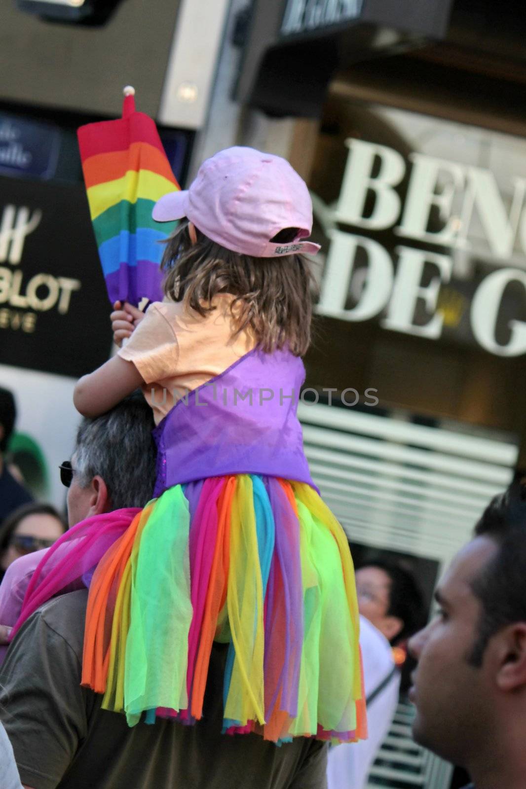 Little girl sitting on a man's shoulders, wearing a cap and a multicolored skirt and holding the rainbow flag at the Gay Pride 2011, Geneva, Switzerland