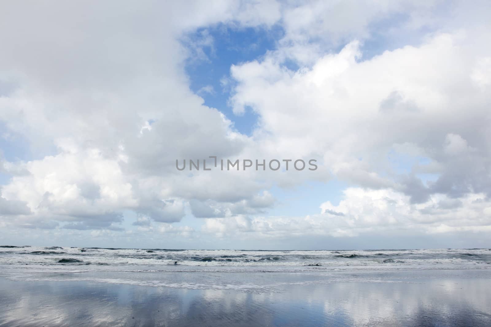 clouds and blue sky reflected in wet beach by ahavelaar