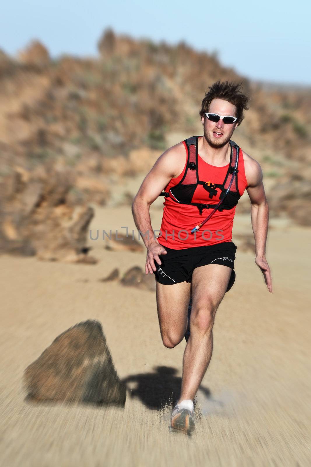 Runner. Man running fast in dramatic desert landscape. Fit fitness trail runner sprinting at high speed. Caucasian male model outside.