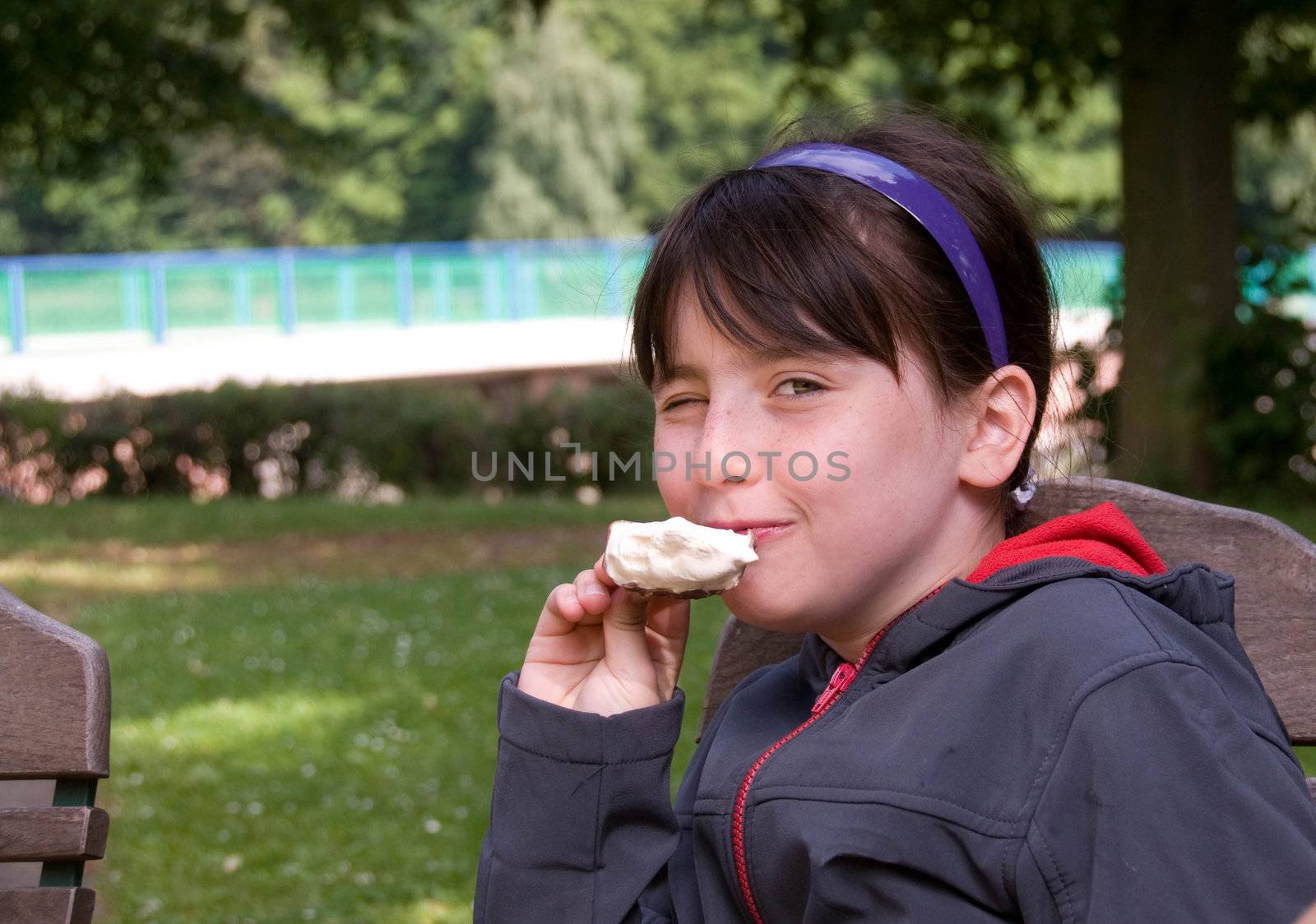 Freckled girl eating ice cream, smiles and winks.