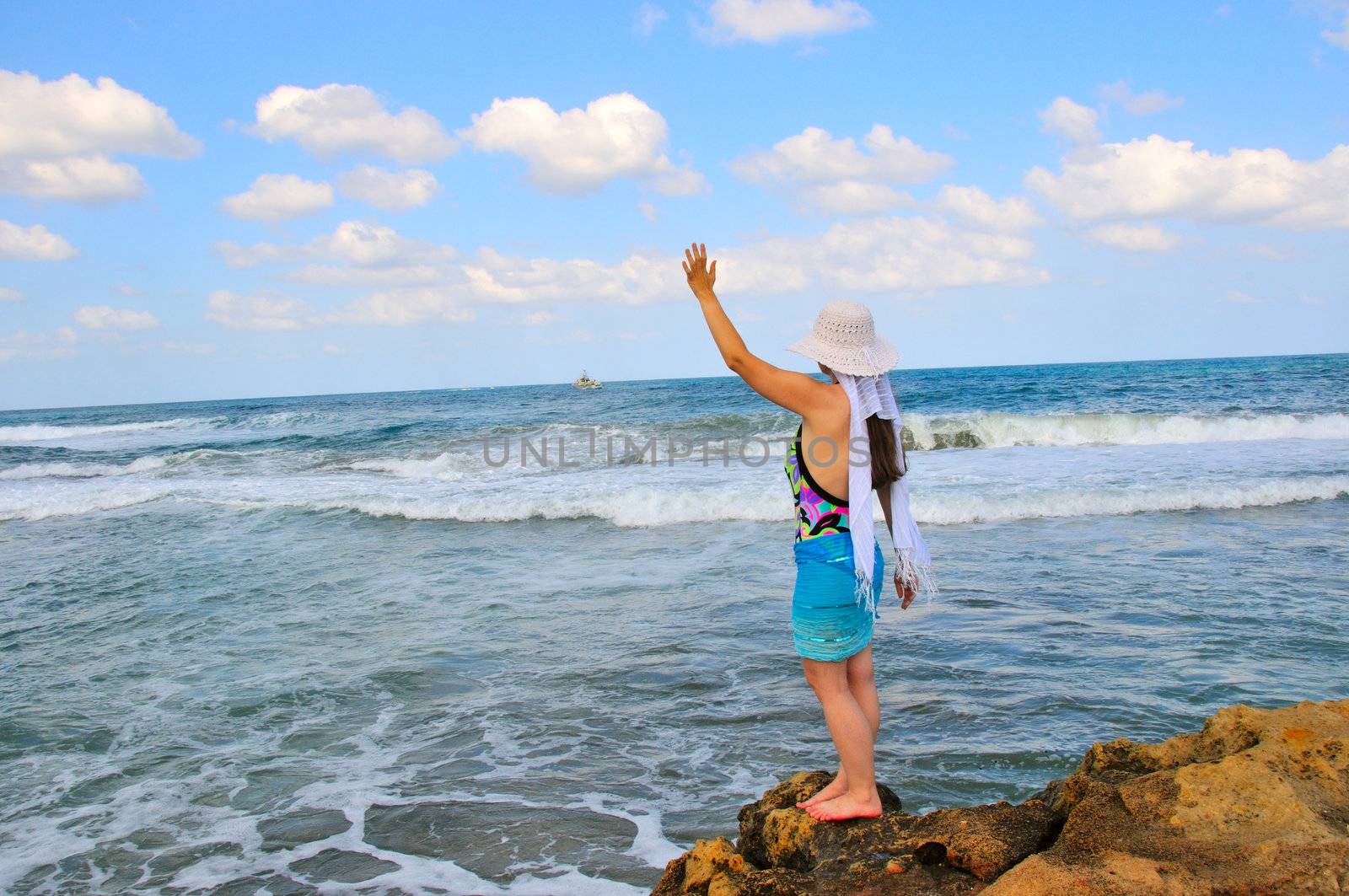 A girl stands on the shore and waving the departing ship